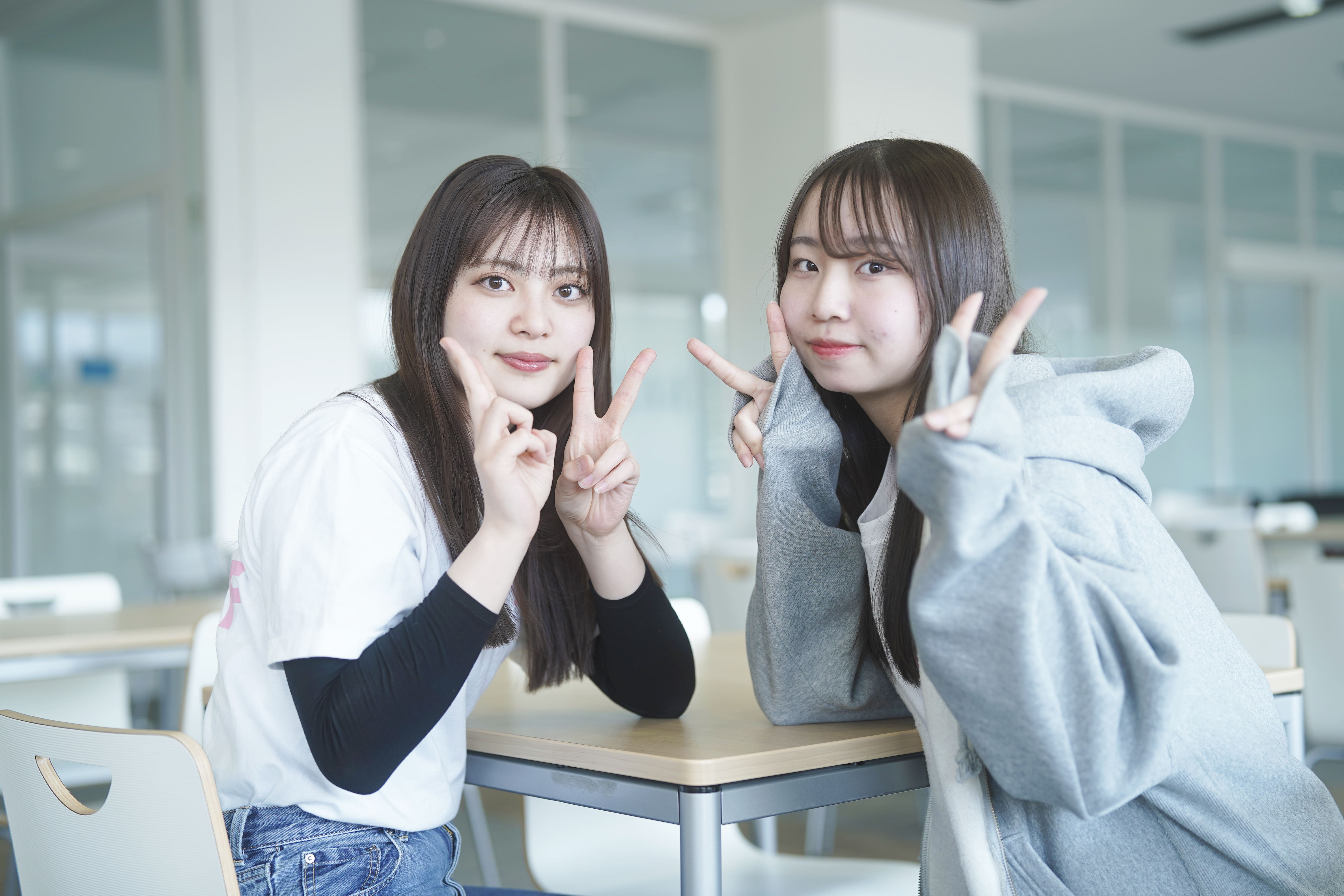 座って笑顔でピースをする2人の女子大学生